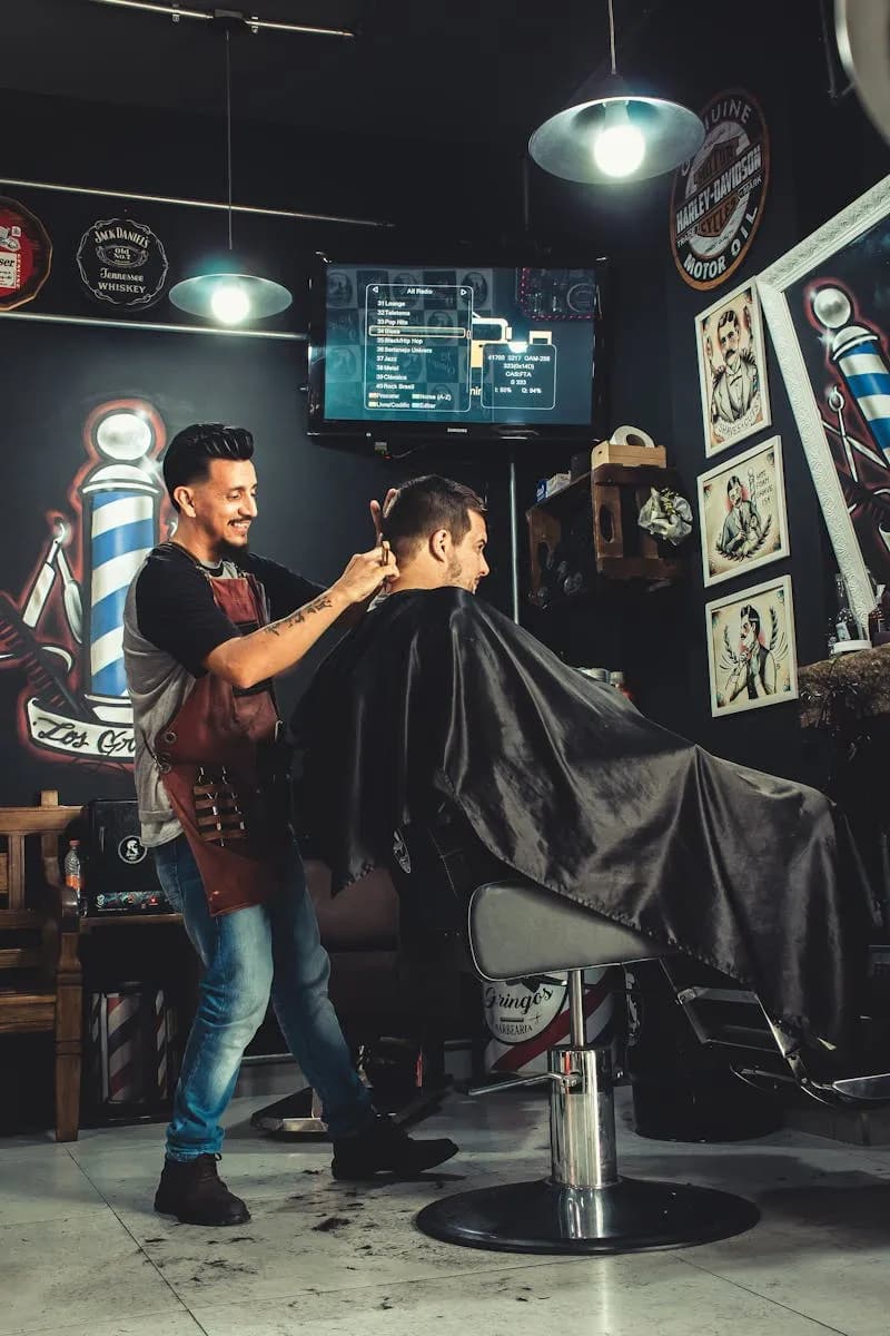 Barbero sonriendo mientras corta en barbería oscura