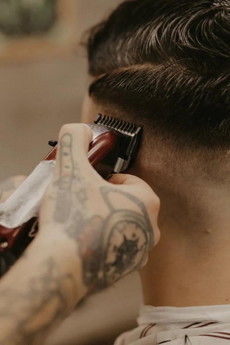 Close-up de clipper marcando fade con manos tatuadas